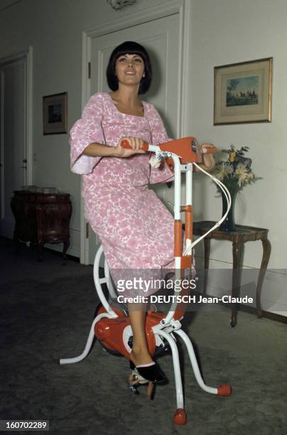 Close-up Of Mireille Mathieu In Gdr . RDA-1972 - Mireille MATHIEU, en chemise de nuit à fleurs roses, mules aux pieds, fait du vélo d'appartement,...