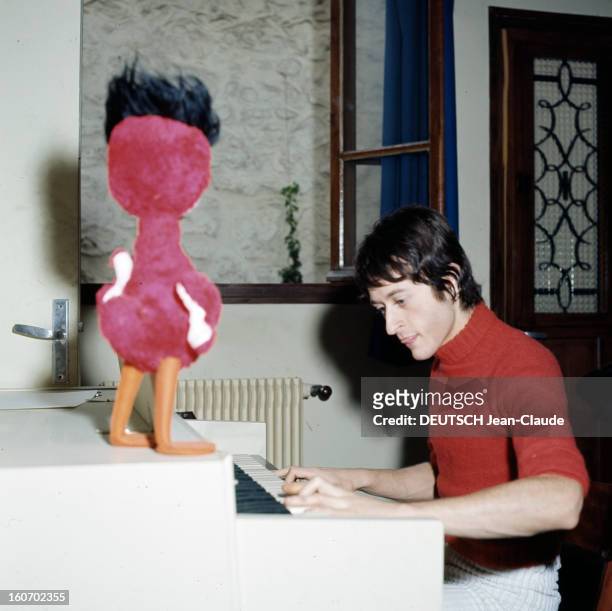 Michel Polnareff With Brown And Short Hair. En 1967, Michel POLNAREFF, les cheveux courts et bruns, vêtu d'un pull à col roulé rouge, joue d'un orgue...