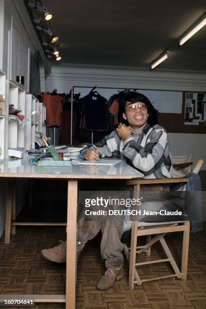 Close-up Of Kenzo Takada. En novembre 1975, assis devant un bureau blanc, le styliste KENZO Takada, souriant, portant une chemise à carreaux, un...