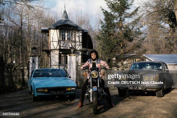 Close-up Of Michel Sardou. En France, en mars 1974, chez lui devant sa maison, vêtu d'un pantalon noir, d'un pull à col roulé noir, d'un blouson...