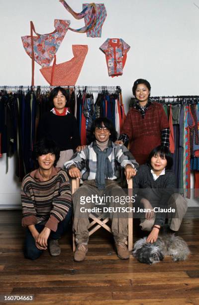 Close-up Of Kenzo Takada. En novembre 1975, assis sur une chaise, devant des vêtements suspendus à des tringles et au mur, le styliste KENZO Takada,...