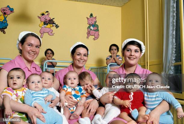 The Old France In Year 2000. Dans une crèche, trois nurses en tenue professsionnelle, blouse rose et couvre-chef en coton blanc, tiennent dans leurs...