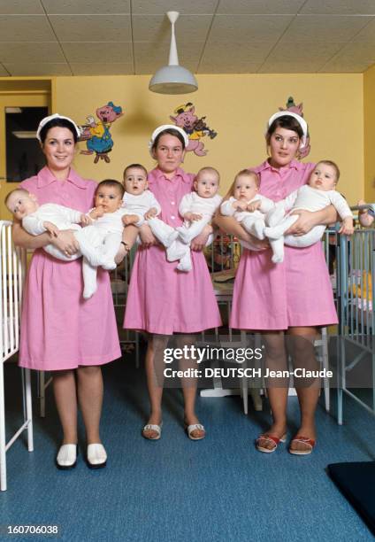The Old France In Year 2000. Dans une crèche, trois nurses en tenue professsionnelle, blouse rose et couvre-chef en coton blanc, tiennent debout,...