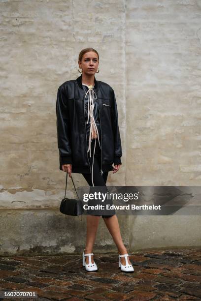 Guest wears gold earrings, a gold chain pendant necklace, a black satin with beige borders jacket, a black shiny leather bomber jacket, black knees...