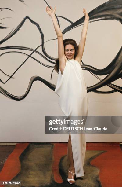 Summer Fashion By Couture Designers. Un mannequin femme, devant un mur blanc calligraphié en noir, pose bras levés en haut, dans une robe longue...