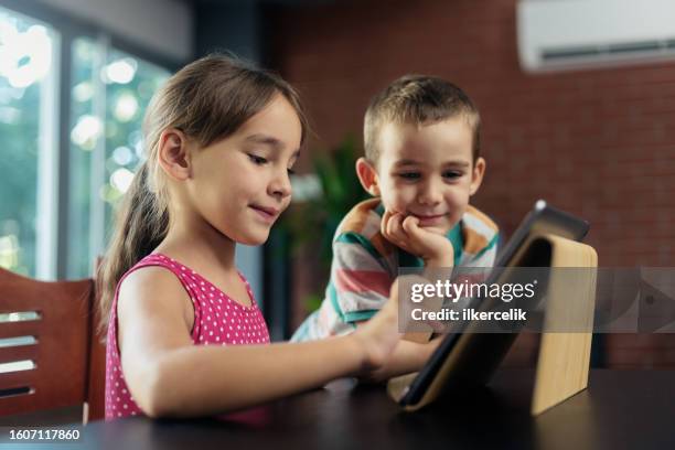 kleiner bruder und schwester spielen videospiel auf digitalem tablet zu hause - grundschüler stock-fotos und bilder