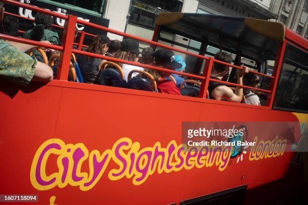 Visitors to the capital enjoy sunshine on the top deck oif their 'City Sightseeing' tour bus at Haymarket in the West End, on 16th August 2023, in...