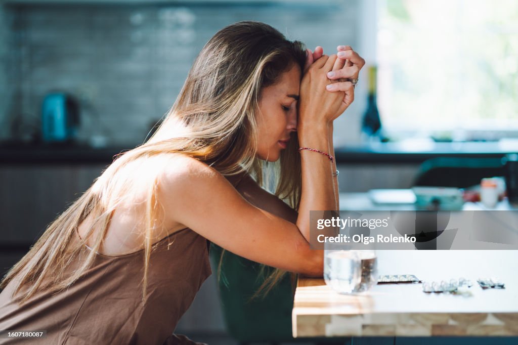 Domestic violence and women mental illness. Crying woman with head in hands drinking pills on the kitchen