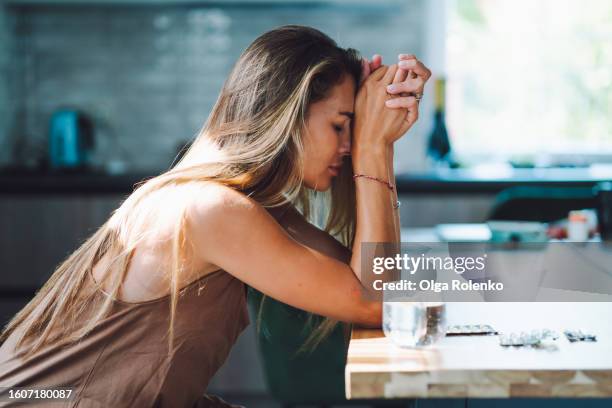 domestic violence and women mental illness. crying woman with head in hands drinking pills on the kitchen - sad woman stock pictures, royalty-free photos & images