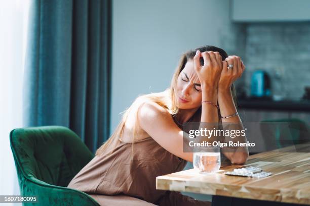 loneliness and break up aftermath. crying woman with head in hands drinking pills on the kitchen - hangover headache stock pictures, royalty-free photos & images