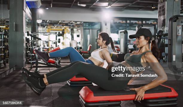 two young woman doing knee tuck crunches in the gym. powerful female bodybuilder pumping abs muscles. - asian female bodybuilder stock pictures, royalty-free photos & images