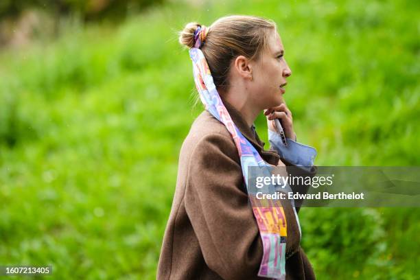 Guest wears a multicolored print pattern silk scarf as a hair elastic, a brown wool long coat, outside OperaSport, during the Copenhagen Fashion Week...