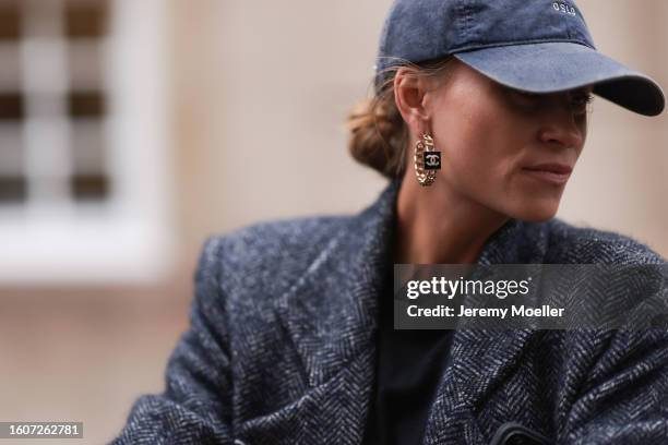 Tine and rea wears a denim cap, Chanel gold and black hoops and earrings, black cotton t-shirt, grey houndstooth pattern long coat, outside The...