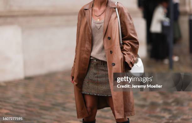 Darja Barannik wears gold necklaces, Prada beige wool knit tank top, brown leather coat, brown checked short skirt, Prada white leather bag, black...