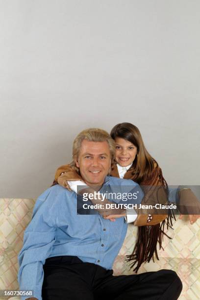 Thierry Roussel And Daughter Athina Pose In Studio. Thierry ROUSSEL, assis sur un canapé, sa fille Athina, avec une veste western à franges, le...
