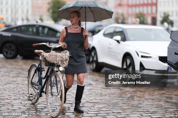 Guest wears white pearl necklaces, grey short strap dress with pockets, white wool high socks, black leather high boots and a black umbrella, outside...