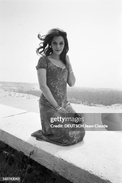 Tina Aumont Shows Spring 1971 Paris Fashion In Tunisia. En Tunisie, à Nefta, Tina AUMONT, agenouillée sur un muret, dans un paysage aride, présentant...