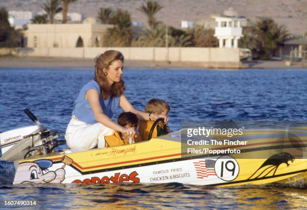 Queen Noor al Hussein of Jordan with her sons, Prince Hashim and Prince Hamzah, driving an outboard motorboat off the coast of their Red Sea Palace...