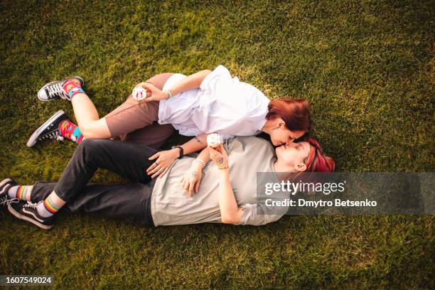 happy lesbian couple romancing lying on the grass during summer - beso en la boca fotografías e imágenes de stock