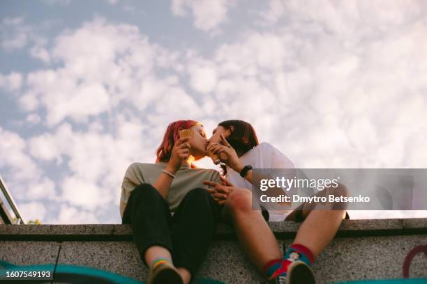 lesbian couple kissing while sitting in the city during summer - lesbian date stock-fotos und bilder