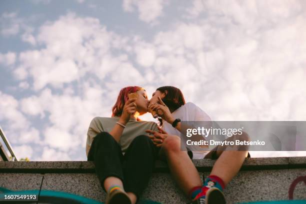 lesbian couple kissing while sitting in the city during summer - beso en la boca fotografías e imágenes de stock
