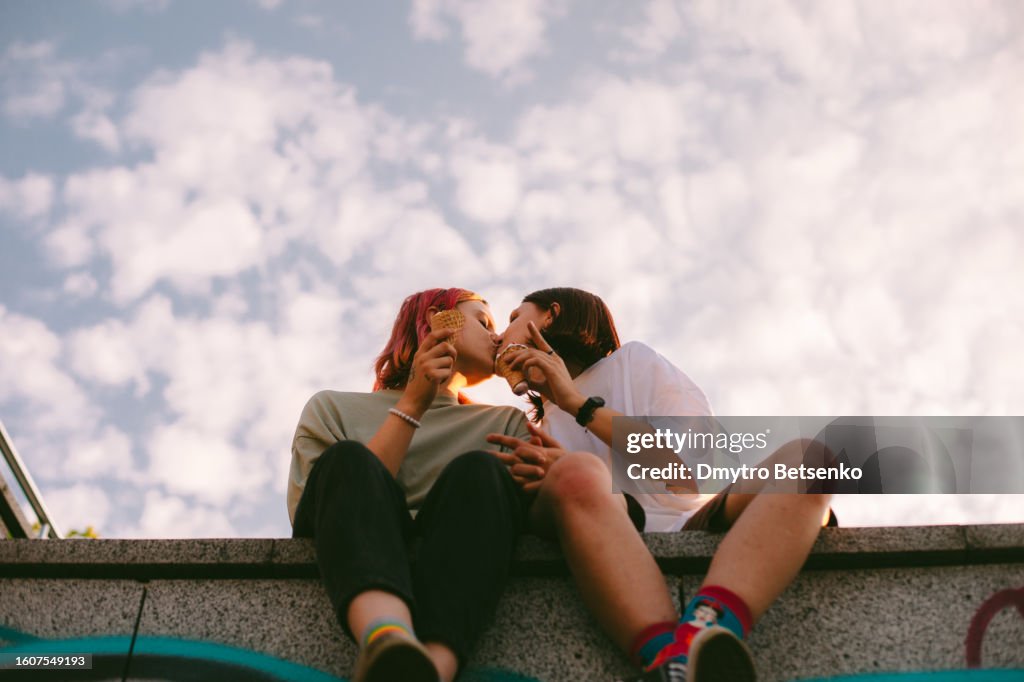 Lesbian couple kissing while sitting in the city during summer