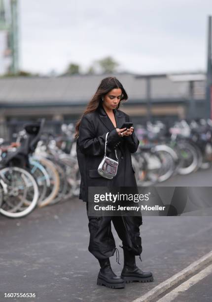 Naomi Anwer seen wearing silver earrings, black oversized blazer, matching black cargo pants, silver metallic bag and Copenhagen Studios CPH685...