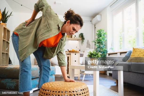 young woman experiencing backache, while doing chores in the house - bending stock pictures, royalty-free photos & images