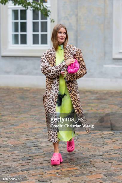 Guest wears animal print coat, pink bag, crocs, yellow dress outside Marimekko during the Copenhagen Fashion Week Spring/Summer 2024 on August 09,...