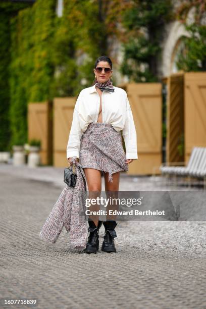 Gili Biegun wears brown sunglasses, gold earrings, a beige and burgundy Dior Oblique Jacquard print pattern silk scarf from Dior, a white open cotton...