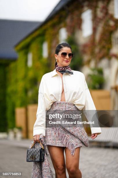 Gili Biegun wears brown sunglasses, gold earrings, a beige and burgundy Dior Oblique Jacquard print pattern silk scarf from Dior, a white open cotton...