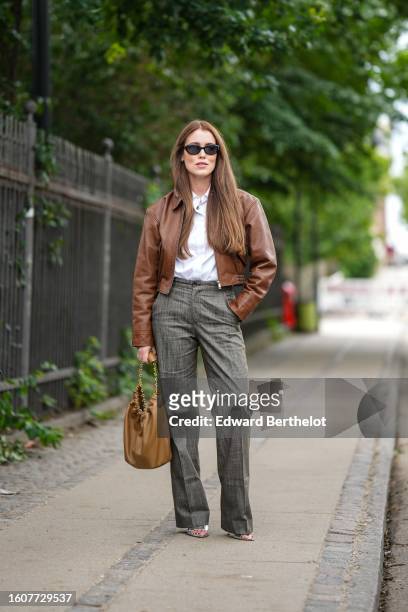 Annabel Rosendahl wears black sunglasses, a white shirt, a camel shiny leather zipper jacket, gray wide legs suit pants, a brown shiny leather Chanel...