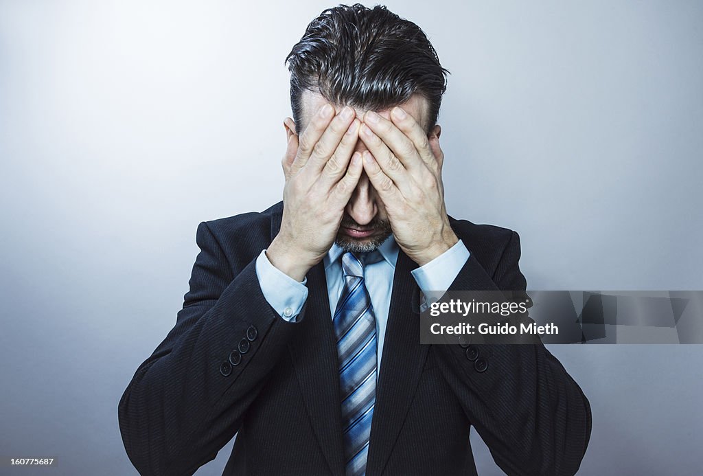 Business man with hands in front of face.