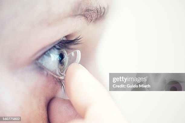 close up of woman putting in contact lens - lenti a contatto foto e immagini stock