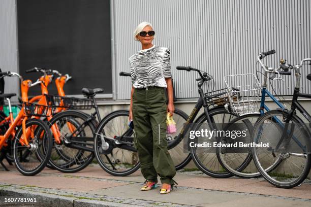 Grece Ghanem wears black sunglasses, a purple wool pullover knot at the shoulder, a black and white zebra print pattern short sleeves t-shirt, khaki...