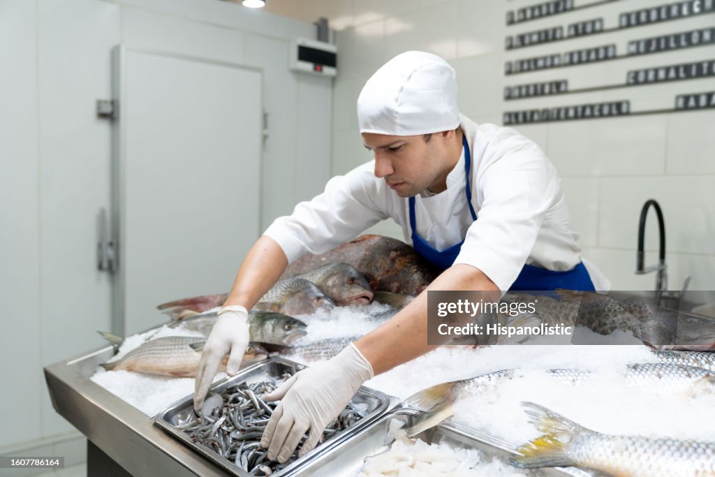 Caucasian fishmonger organizing a container with sardines on ice display at a fish market