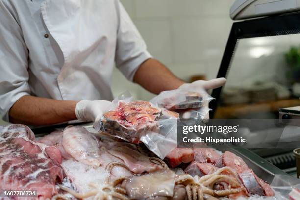 unrecognizable vendor holding fish slice in a vacuum sealed package at a sea food market - airtight stock pictures, royalty-free photos & images