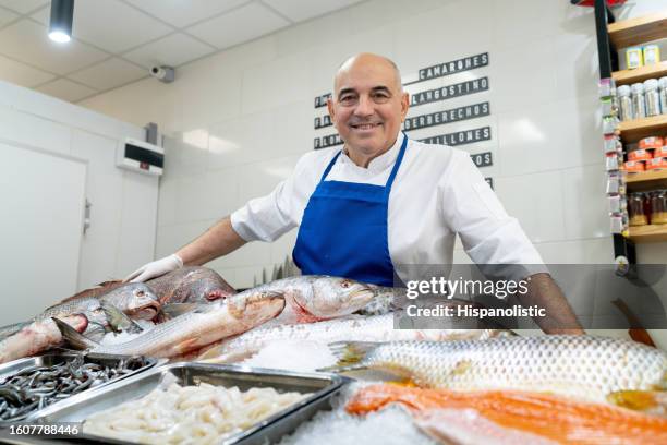 maturo proprietario maschio di un mercato del pesce in piedi dietro il bancone del pesce mentre sorride alla telecamera - pescivendolo foto e immagini stock