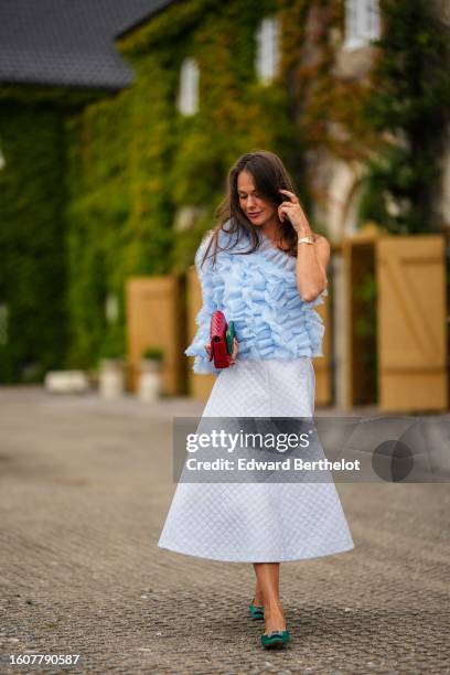Therese Hellström wears a pale blue ruffled tulle asymmetric shoulder / one sleeves blouse, a white embossed pattern midi puffy skirt, a red shiny...