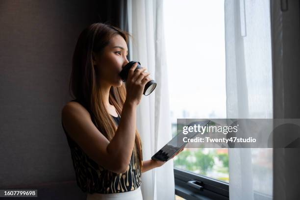 asian businesswoman drinking a coffee and holding a digital tablet in the hotel room - man in suite holding tablet stock-fotos und bilder