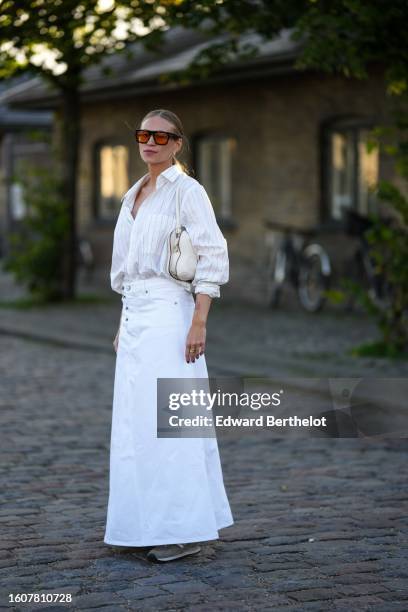 Tine Andrea Lauvli wears black and orange sunglasses, a white striped print pattern shirt, a white denim long skirt, a beige matte leather shoulder...