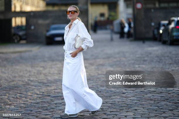 Tine Andrea Lauvli wears black and orange sunglasses, a white striped print pattern shirt, a white denim long skirt, a beige matte leather shoulder...