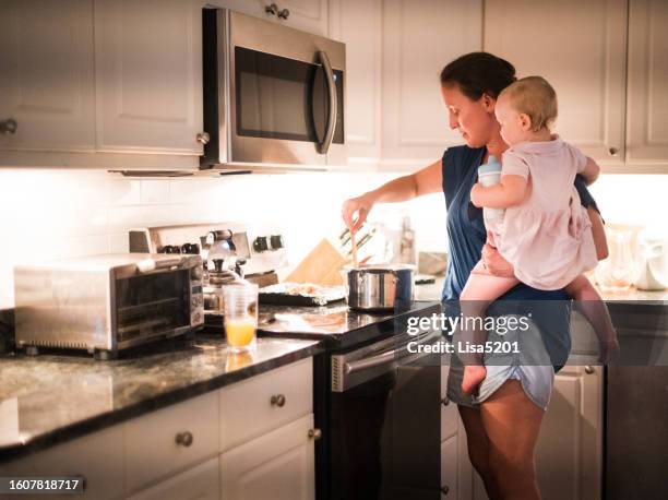 mujer en casa cocinando mientras sostiene a un niño pequeño en la cocina familiar - típico de clase mediana fotografías e imágenes de stock