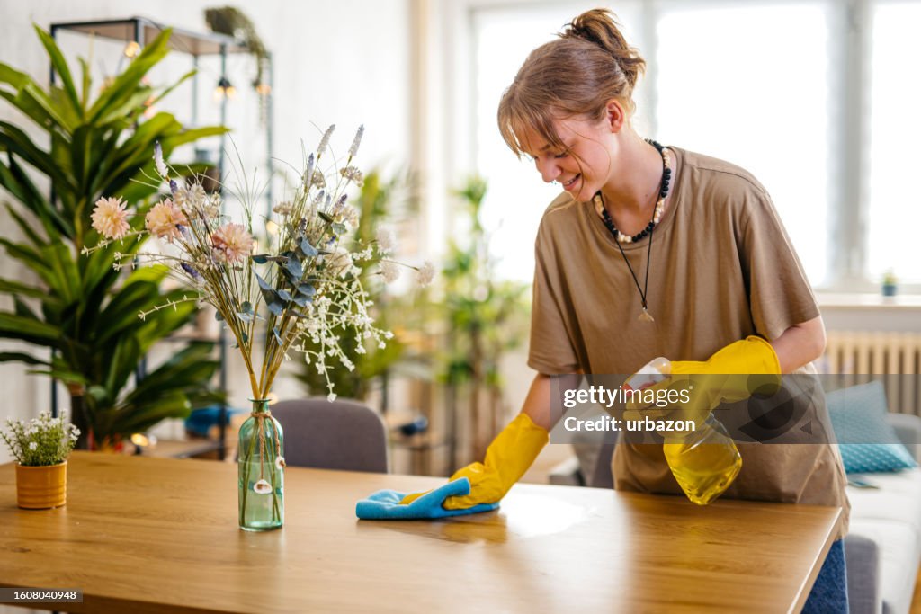 Mulher nova limpando a superfície da mesa de jantar