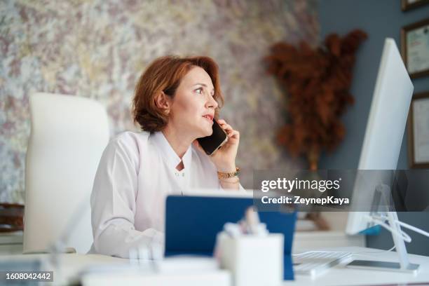 the female doctor is talking on the phone at her office desk - dermatologists talking to each other patient stock pictures, royalty-free photos & images