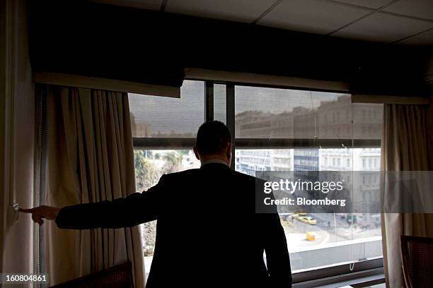 Yannis Stournaras, Greece's finance minister, raises the blinds in his office to reveal an old bullet hole in the window, following a Bloomberg...