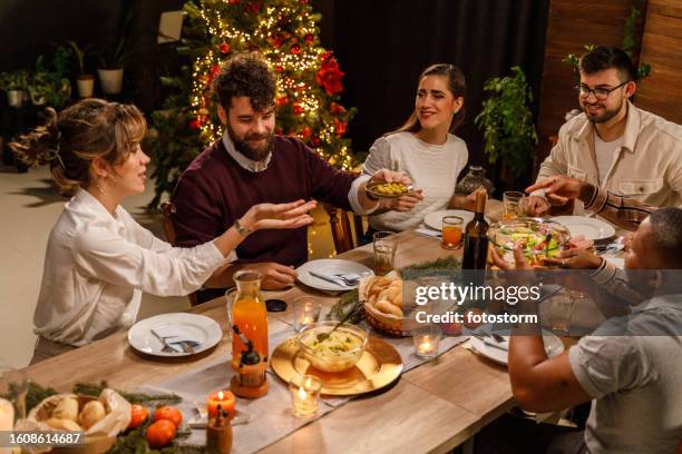 friends enjoying drinks, delicious food and chatting casually during a christmas dinner party - large dinner party stock pictures, royalty-free photos & images