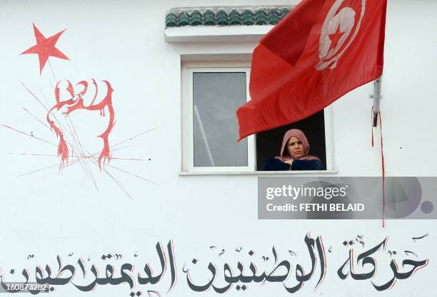 Tunisian woman watches behind a national flag as mourners pour into Jebel Jelloud, a suburb of Tunis and hometown of assassinated leftist leader...