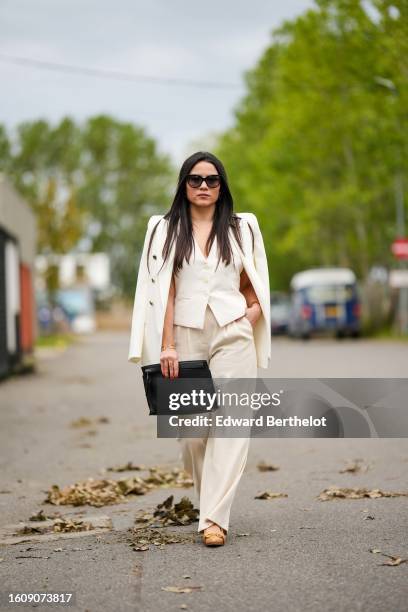 Guest wears black sunglasses, a white latte buttoned sleeveless gilet, a white latte shoulder-pads blazer jacket, matching white latte suit pants, a...