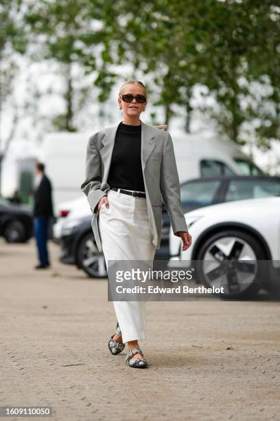Guest wears black marble pattern sunglasses from Chanel, gold earrings, a black turtleneck ribbed pullover, a pale gray oversized blazer jacket, a...
